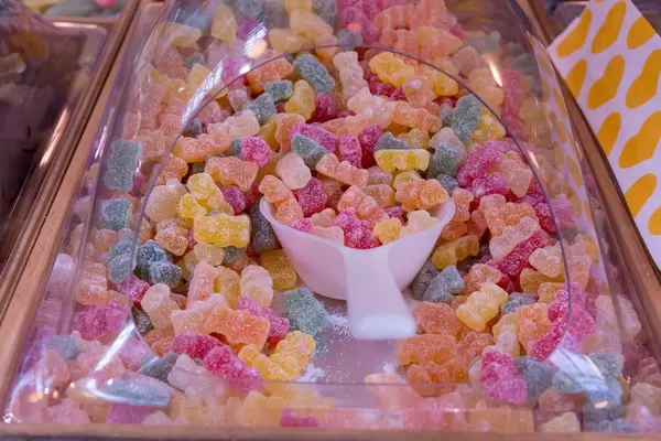 Nahaufnahme von mit Zuckerpulver überzogenen Gummibärchen in Süßigkeitenbox mit Schaufel