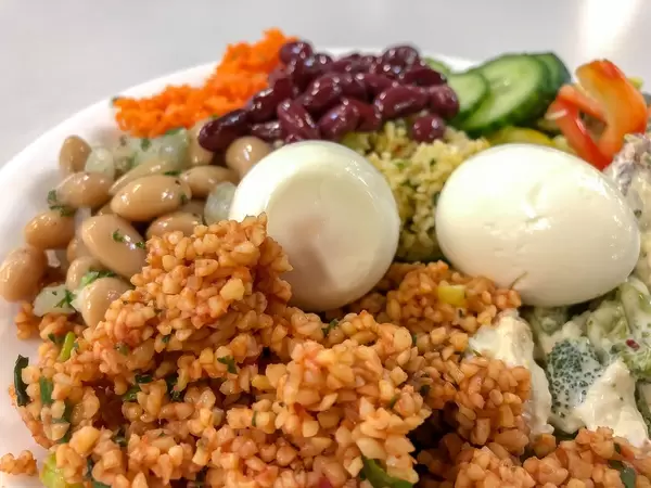 Nahaufnahme von nahrhaftem Salat mit Couscous, ganzem Ei, Bohnen, Gurken und Karotten