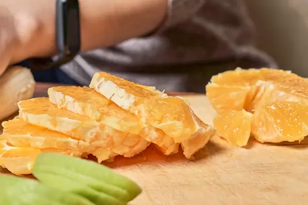 Nahaufnahme von Orangenscheiben auf einem Holzbrett mit Mann, der im Hintergrund schneidet