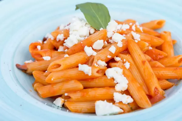 Nahaufnahme von Penne mit Tomatensoße und geriebenem Fetakäse