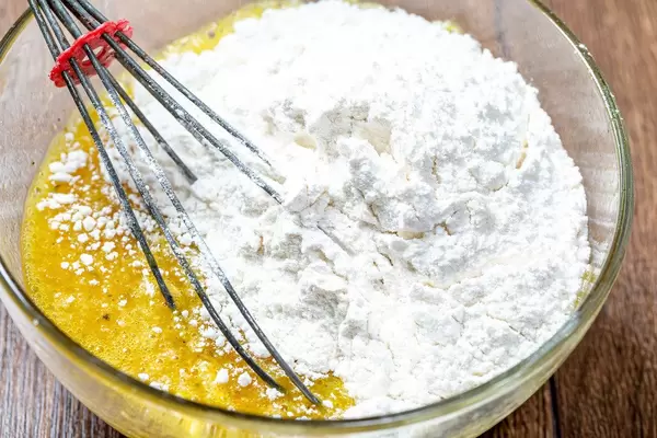 Nahaufnahme von roher Eimaße in einer Glasschale, mit Mehl und einem Schneebesen, um Keksteig zum Backen zuzubereiten