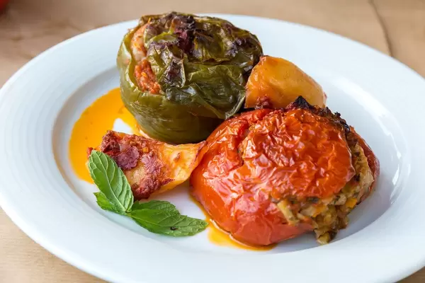 Nahaufnahme von schrumpeligen gefüllte Tomate, mit Paprika, mit mediterraner Reisfüllung, Pinienkerne, Rosinen und Minze, auf einem weißen Teller