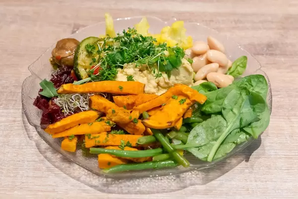 Nahaufnahme von veganem Salat auf Glasteller mit Edamame, Blumenkohl, Spinat, Rote Beete, Pilze und Zucchini