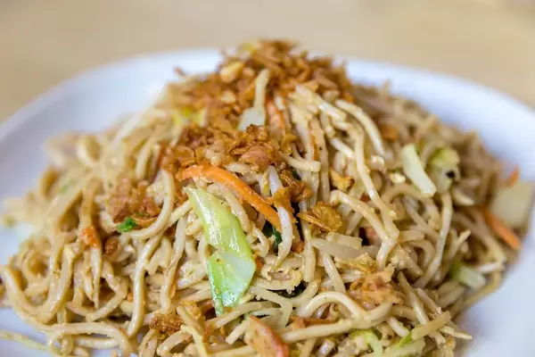 Nahaufnahme von vegetarischen  asiatischen Nudeln, gebratenem Gemüse und Eier-Sauce, auf einem weißen Teller auf einem Holztisch