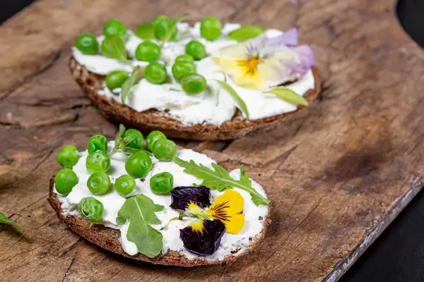 Nahaufnahme von vegetarischen Sandwiches mit Frischkäse, grünen Erbsen, Rukola und essbaren Blumen