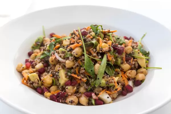 Nahaufnahme von weißem Teller mit Kichererbsen, Avocado, Quinoa, Gemüse. Vegan essen