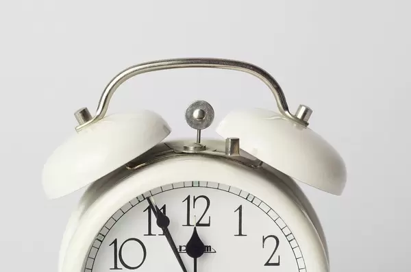 Nahaufnahme von weißem Vintage Wecker kurz vor 12 Uhr vor weißem Hintergrund