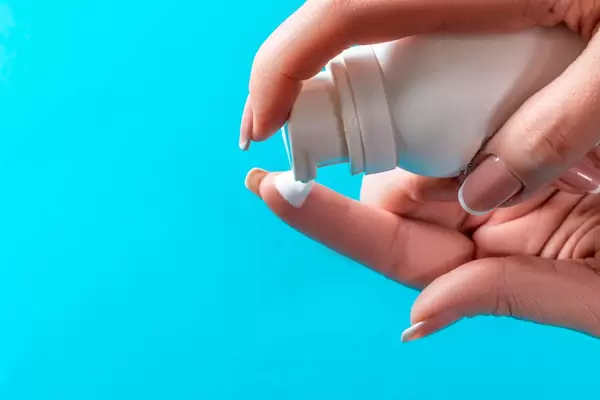 Nahaufnahme Waschschaum aus Kosmetikflasche auf Finger auftragen vor blauem Hintergrund