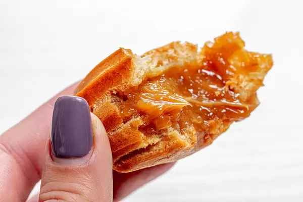 Nahaufnahme zeigt ein Eclair / Hasenpfote mit Füllung in einer Frauenhand