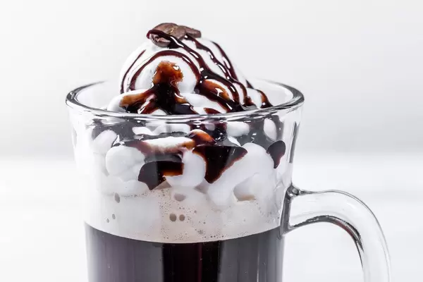 Nahaufnahme zeigt einen Kaffee mit Sahne und Schokosauce im Glas
