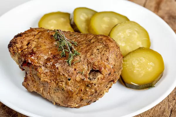 Nahaufnahme zeigt gebackenes Stück Fleisch neben Gewürzgurken