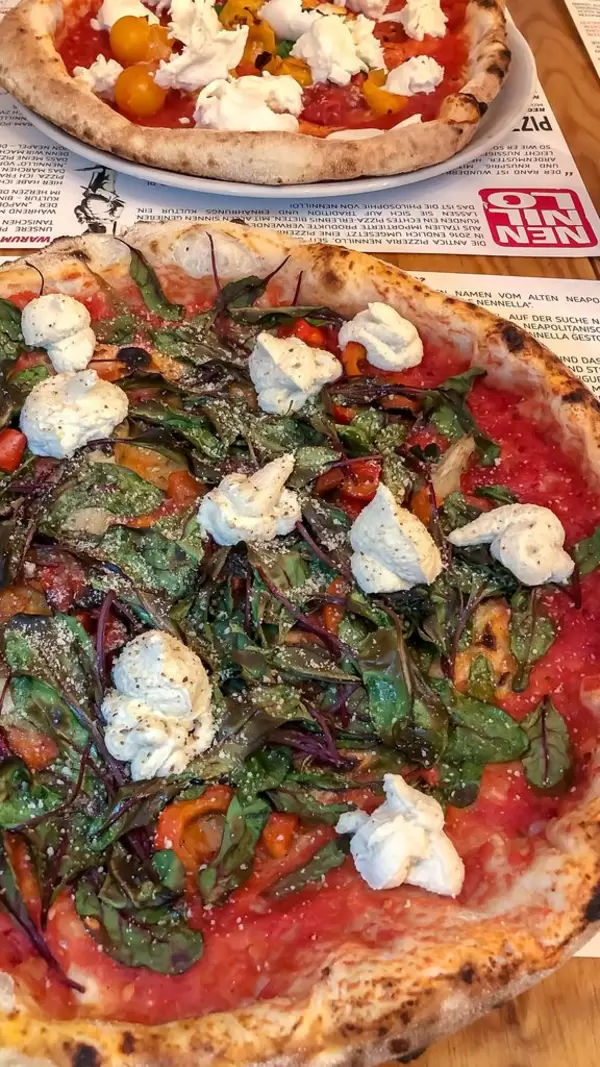 Nahaufnahme zwei Pizzen mit verschiedenen Zutaten auf Tischset in Zeitungs-Optik