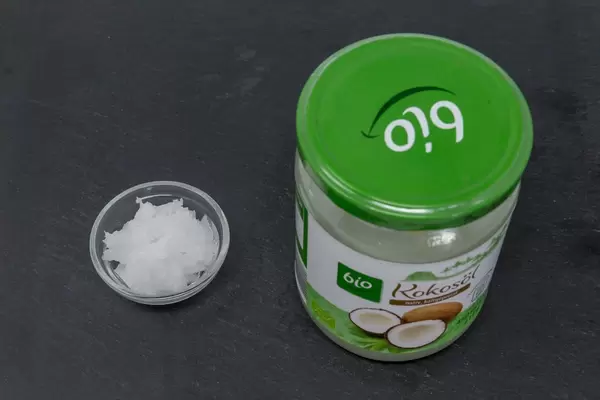 Natives Kaltgepresstes Bio-Kokosöl im Glas mit Muster in Schale daneben auf schwarzer Schieferplatte