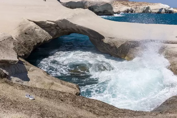 Natural arch and raw sea with no people around and one abandoned sandal on the island of Milos, Greece