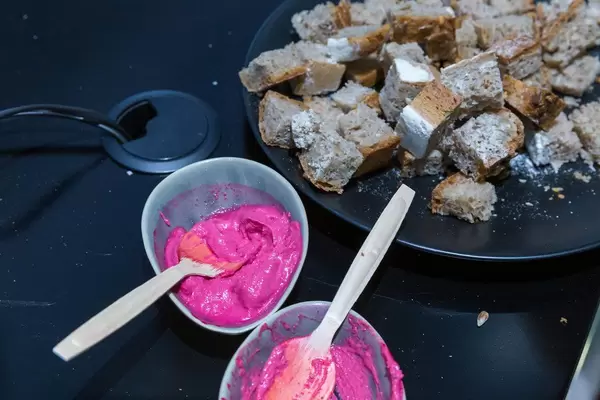 Natürliche pinke Lebensmittel: Rote Beete Hummus in Schälchen und rustikales Brot auf einem schwarzen Teller