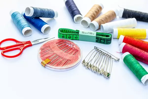 Needles, scissors, measuring tape, pins and thread on white background