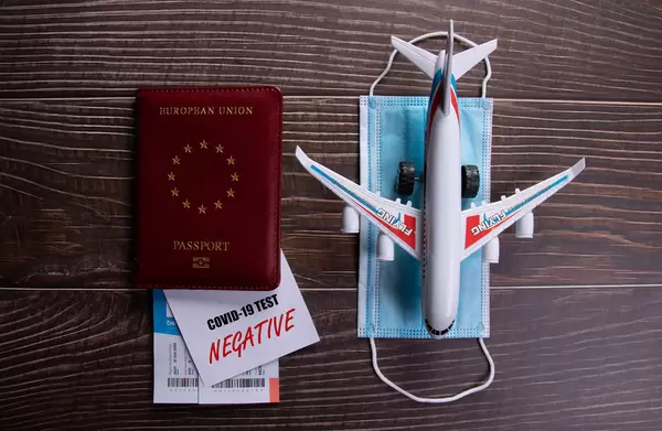 Negative Covid-19 test card with passport, face mask and airplane on wooden table