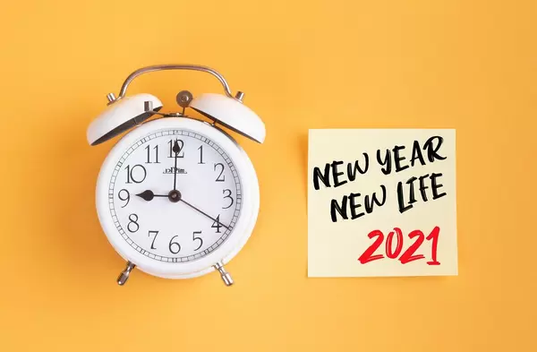 Neue Anfänge: Wecker und ein Zettel mit ‘New year - New life 2021’ Text vor gelbem Hintergrund