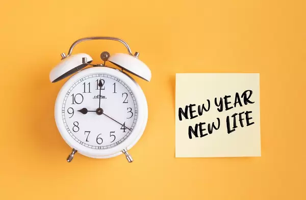 Neue Anfänge: Wecker und ein Zettel mit ‘New year - New life’ Text vor gelbem Hintergrund