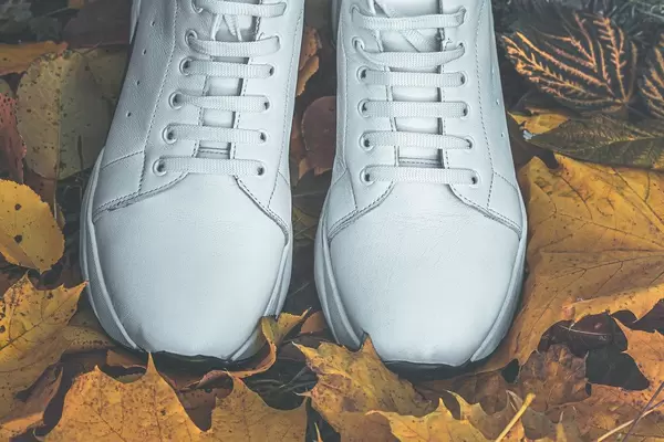 Neue weiße Turnschuhe auf trockenen Herbstgelbblättern