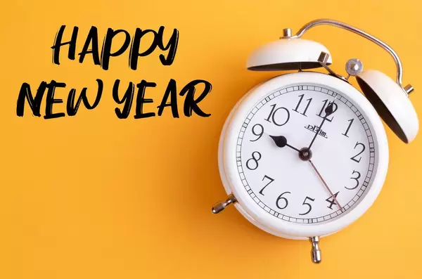 Neues Jahr: Weißer Wecker mit dem Text ‘Happy new year’ vor gelbem Hintergrund