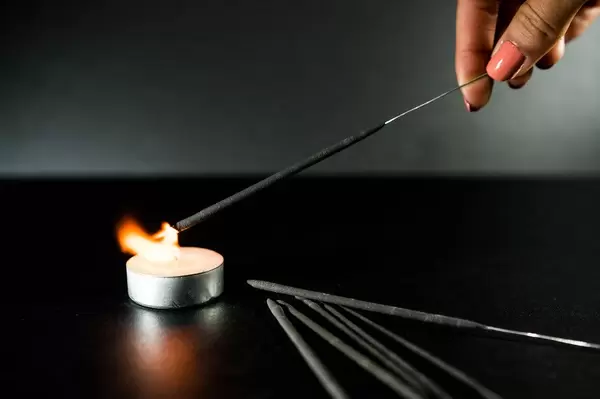 Neujahrsfest - Wunderkerze entzündet sich an der Flamme eines brennenden Teelichts, vor dunklem Hintergrund