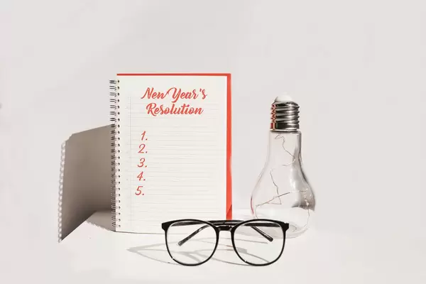 New year's resolution. Desk with notebook, glasses and decorative lamp. White background.