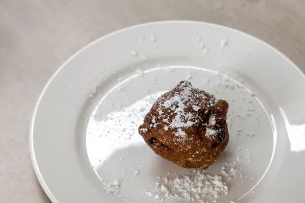 Niederländische Spezialität Oliebol mit Puderzucker bestäubt auf weißem Teller