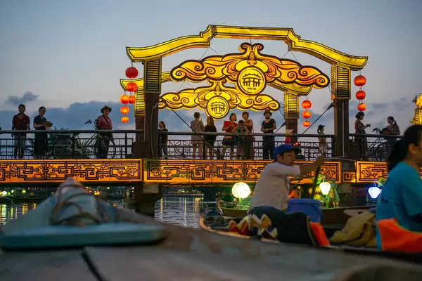 Night Photo from a Wooden Rowing Boat from Tourists standing on the Bridge of Light with Authentic Bright Lanterns in Hoi An, Vietnam