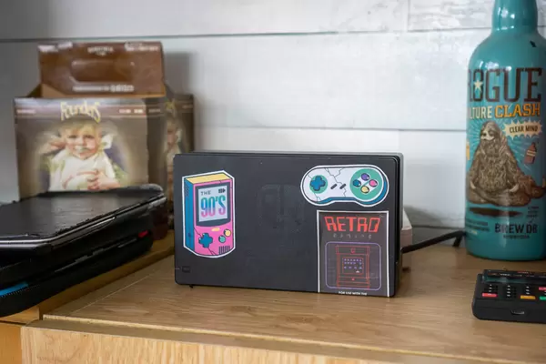 Nintendo Switch Console Dock with Retro Gaming Stickers on a Livingroom Shelf with Games and Remote Control