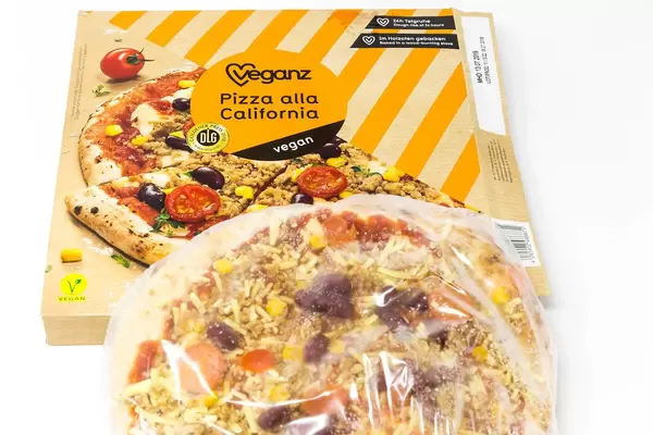 Noch in Plastikfolie eingepackte, vegane Tiefkühlpizza neben Pizzakarton