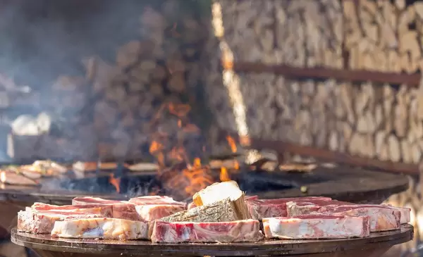 Noch rohe, saftige Koteletts auf runder OFYR Grillplatte und Feuerschale vor Holzscheiten