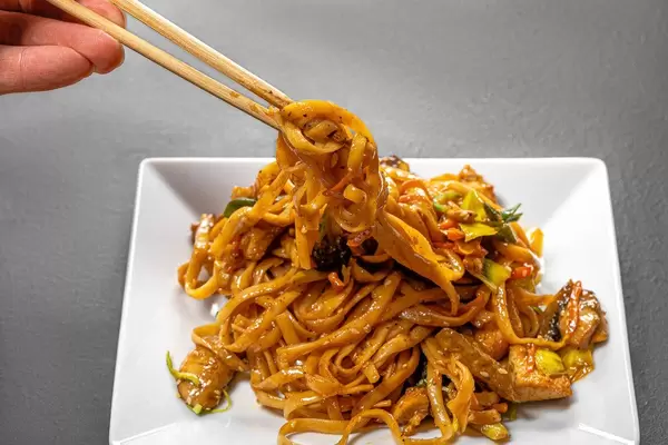 Noodles with vegetables and chicken in a white plate on a black background (Flip 2019)