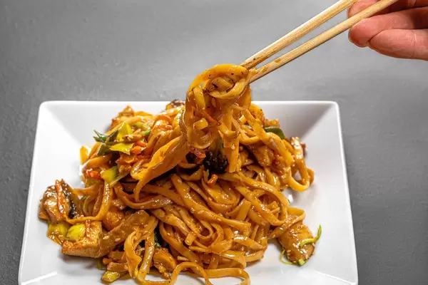 Noodles with vegetables and chicken in a white plate on a black background