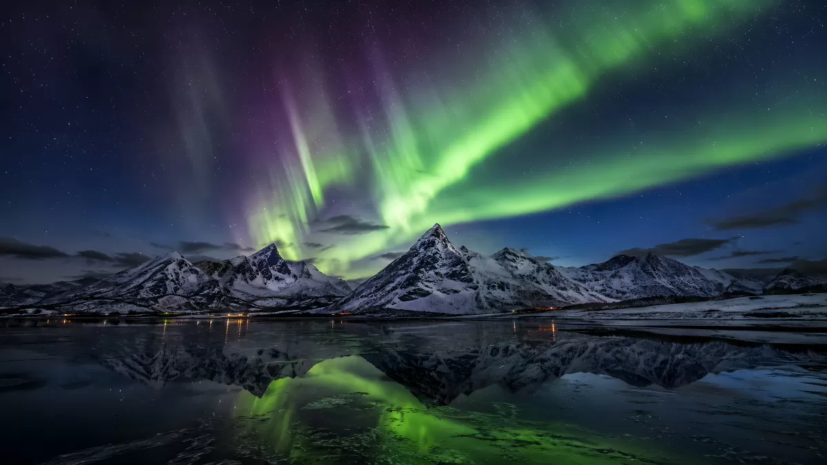 Nordlichter über schneebedeckten Bergen am Fjord