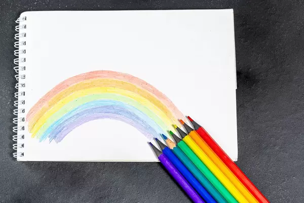 Notebook with painted rainbow and colored pencils on a black background