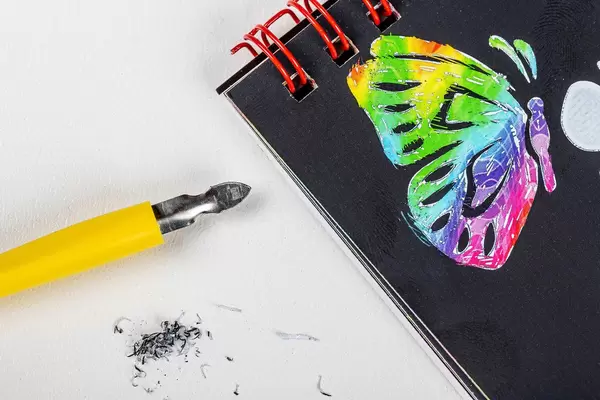 Notepad with a multicolored butterfly drawn and a stichel pen on a white background. Grattage drawing