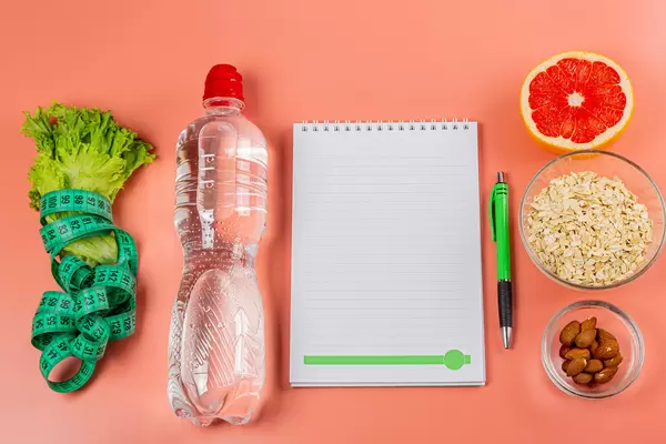 Notepad with pen on pink background with ingredients for healthy and diet food, top view