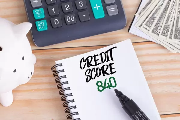 Notizbuch mit Text Credit Score 840, Sparschwein, Taschenrechner und Dollar Geldscheine auf einem Holztisch