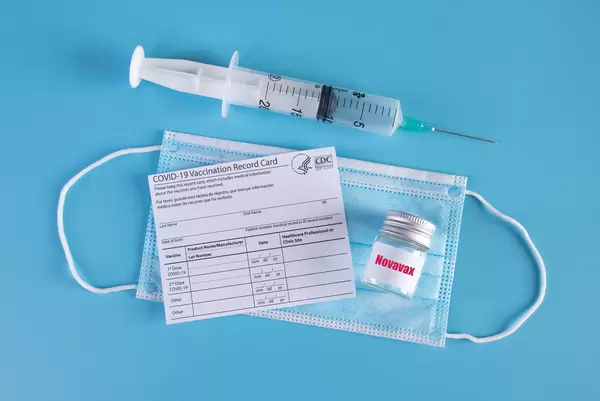 Novavac Covid-19 vaccine with syringe and vaccination record card on blue background