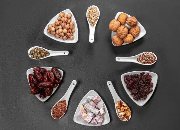 Nuts, seeds, dried dates and candied fruits are arranged in a circle on a black background. Top view (Flip 2019)