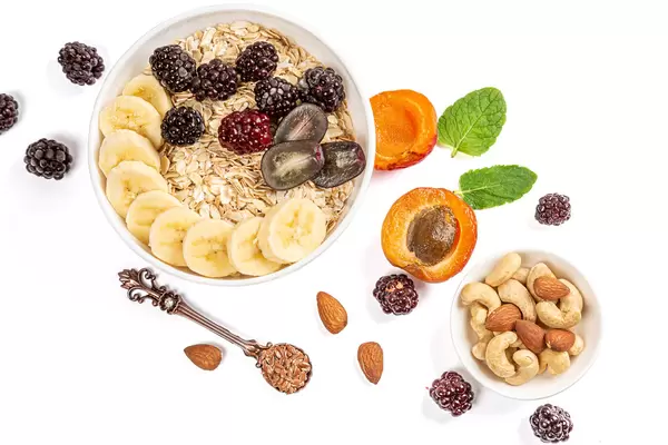 Oat flakes with banana, grapes and blackberries on a white background with apricot, nuts and flax seeds