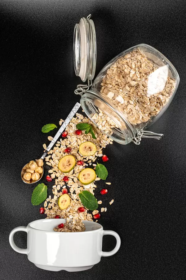 Oat flakes with feijoa pieces, pomegranate, mint and hazelnuts on black background with glass jar and bowl