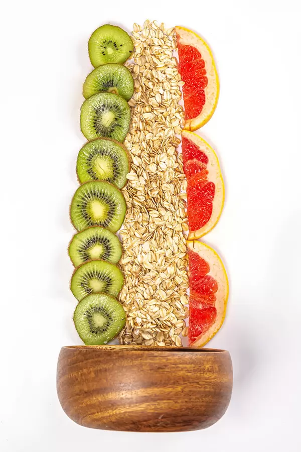 Oat flakes with fresh kiwi and grapefruit slices on white background with wooden bowl