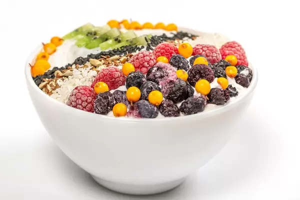 Oat flakes with seeds, berries and coconut flakes in a white bowl, close-up