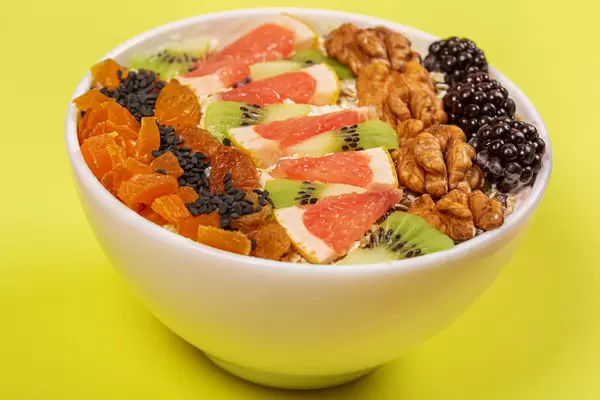 Oat flakes with walnuts and fruit pieces on yellow background