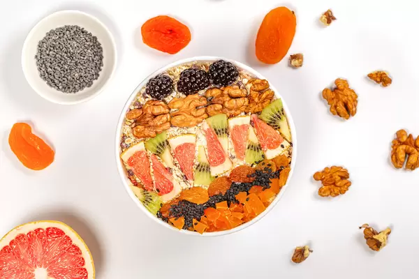 Oat flakes with walnuts and pieces of fruit on white, top view