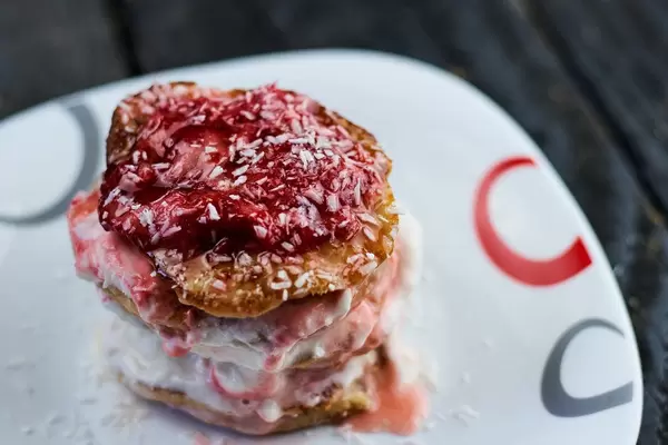 Oat-flour based cake with cream, strawberry jam and coconut flakes on a white plate