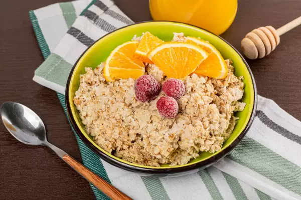 Oatmeal bowl with pieces of orange, raspberry and honey jar