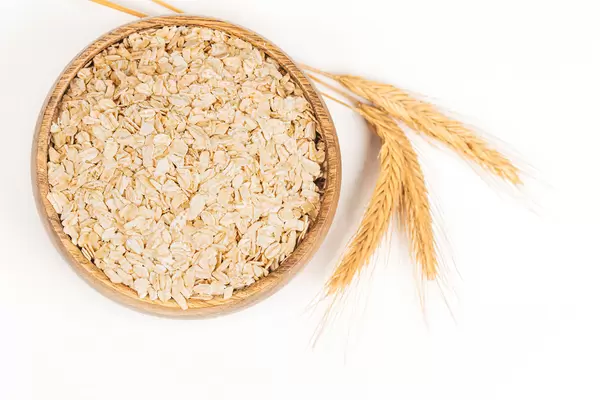 Oatmeal flakes in a round wooden bowl and spikelets on white, top view